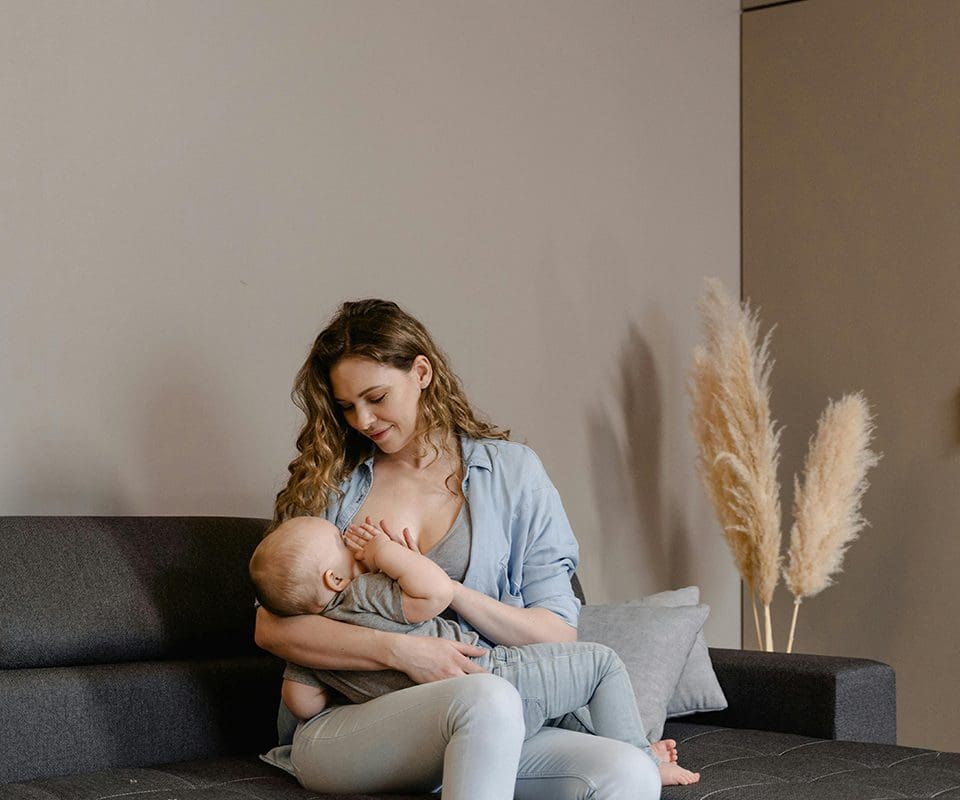 A woman sitting on the couch with her baby.